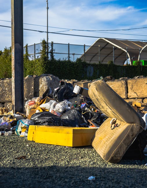 A large pile of black rubbish bags, some appearing to be filled with household waste, is stacked against a modern tiled wall in an outdoor urban setting. Several plastic bottles, including clear water