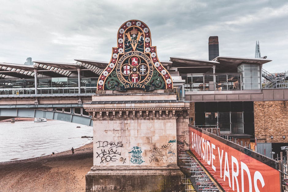 A detailed view of a bridge with a decorative crest mounted on its stone pillar, displaying the logo and insignia of the London County Council, including a crowned shield with various heraldic symbols
