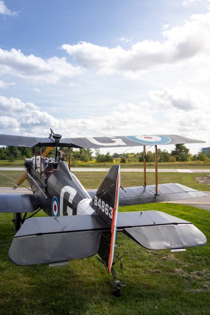 A vintage military aircraft with dark grey metal fuselage and wings, featuring roundel insignia with blue, white, and red concentric circles on the side and upper surfaces of the wings, is parked on a