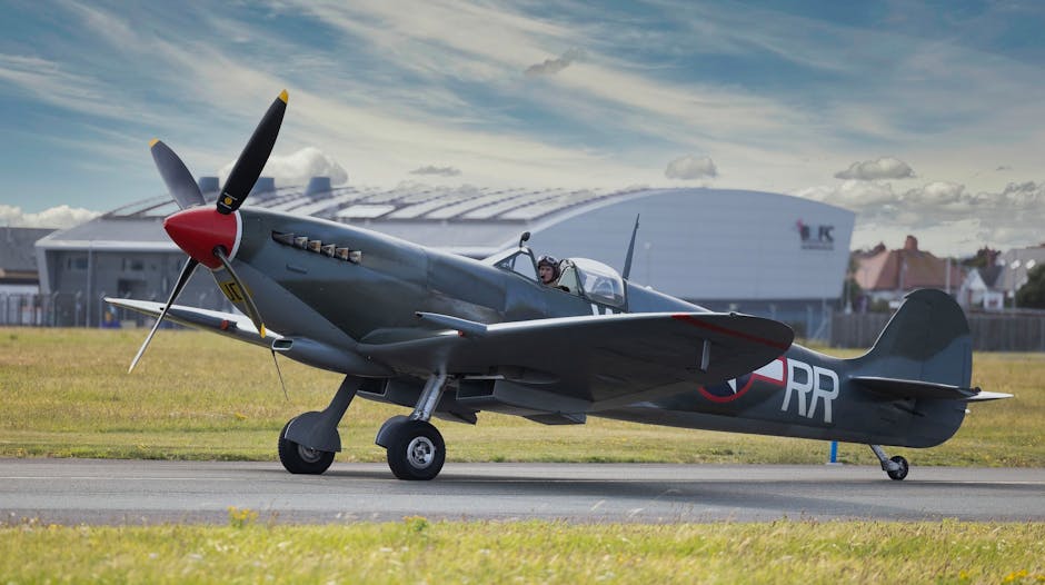 A vintage military aircraft with dark grey metal fuselage and wings, featuring roundel insignia with blue, white, and red concentric circles on the side and upper surfaces of the wings, is parked on a